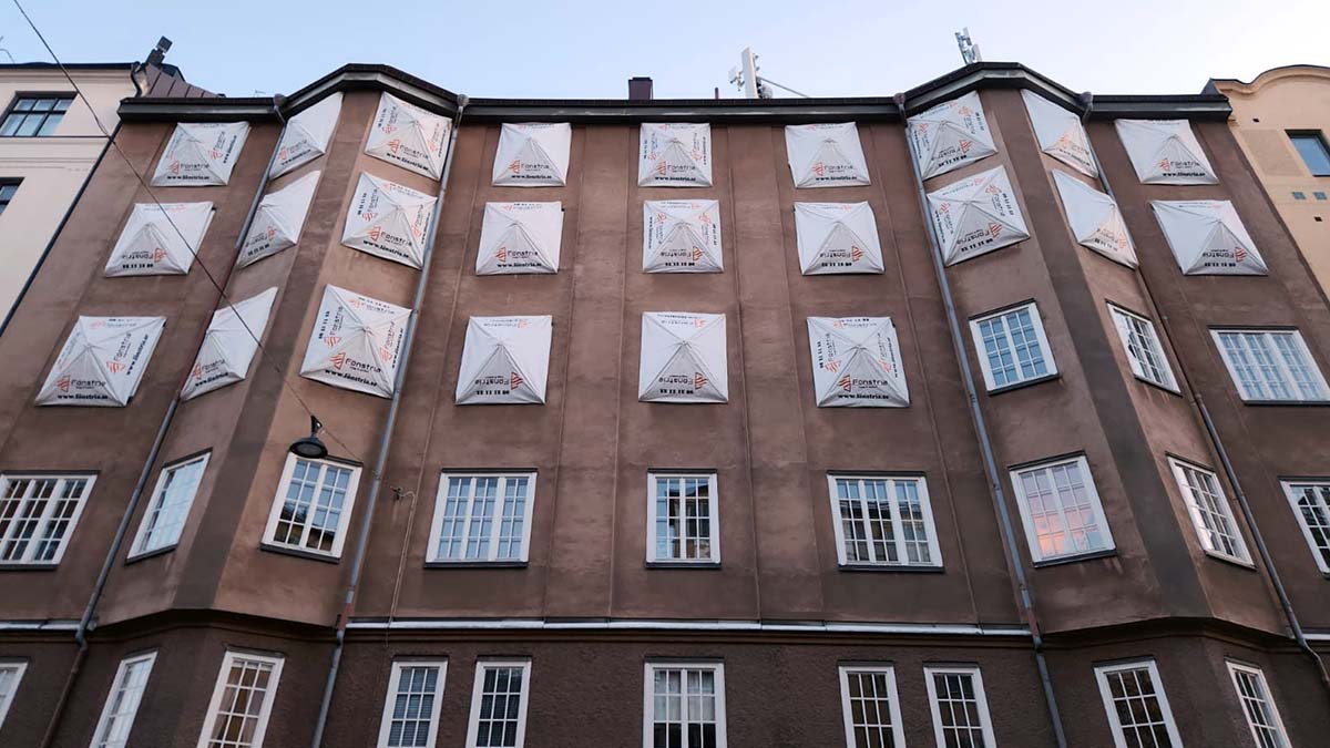 Brun tegelfasad med vita fönster täckta av Fönstria skyddstäckning under pågående totalrenovering på Helenborsgatan 5 i Stockholm